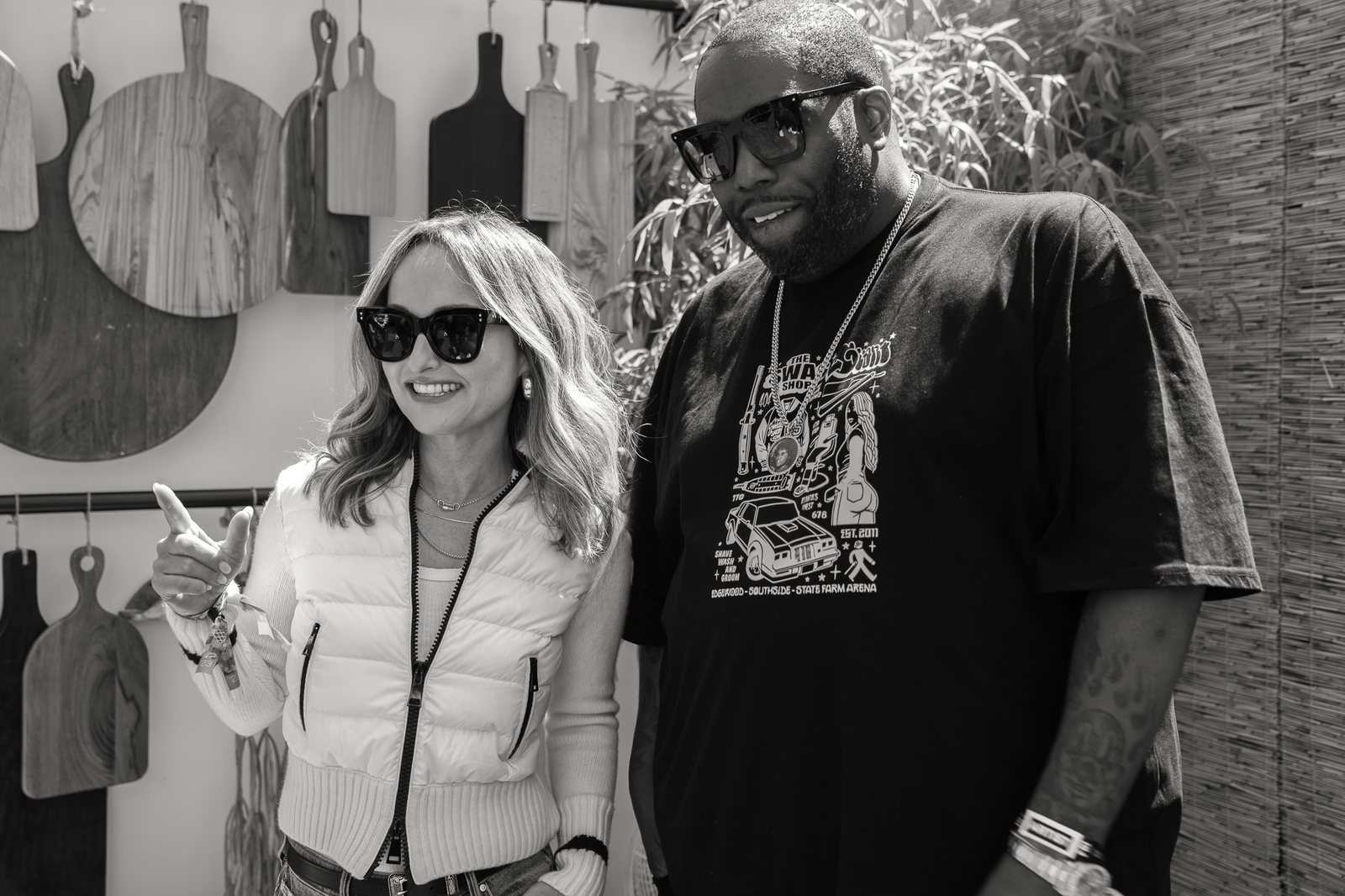 Black and white portrait of two smiling festival guests in sunglasses standing together, photographed by Tara Lenehan