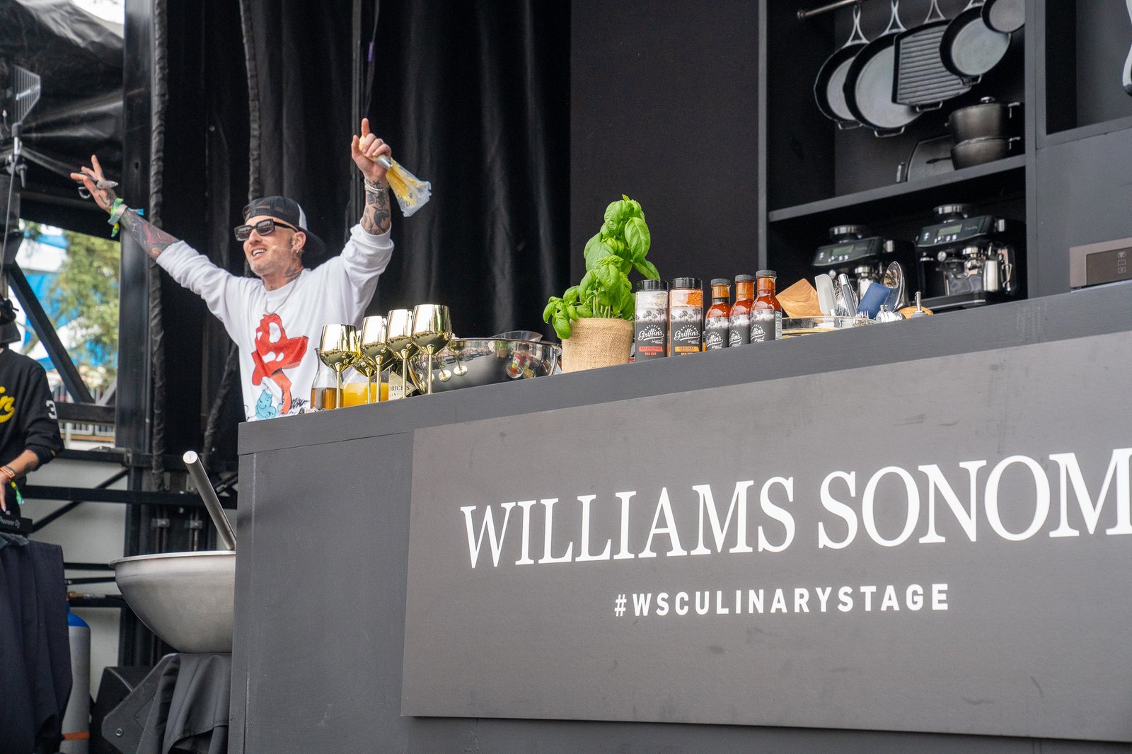 Chef with arms raised on the Williams Sonoma culinary stage at a music festival, photographed by Tara Lenehan