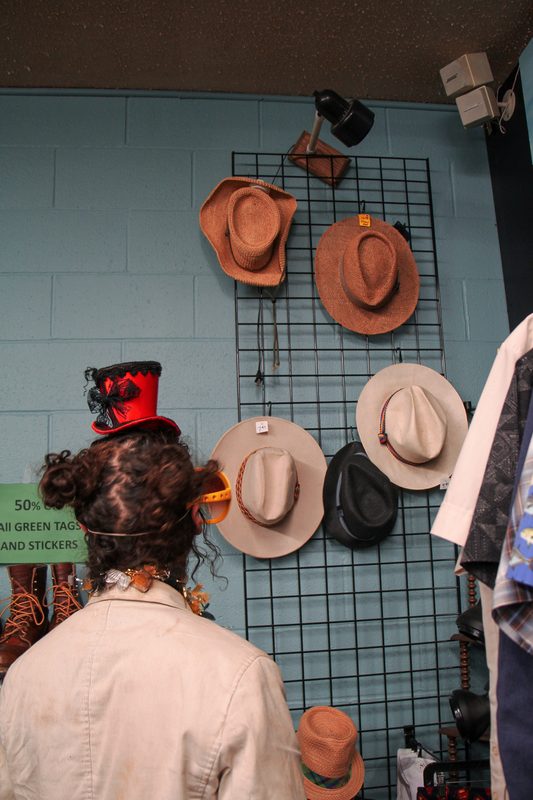 A customer reaching for a felt hat on a wall display inside a small retail shop