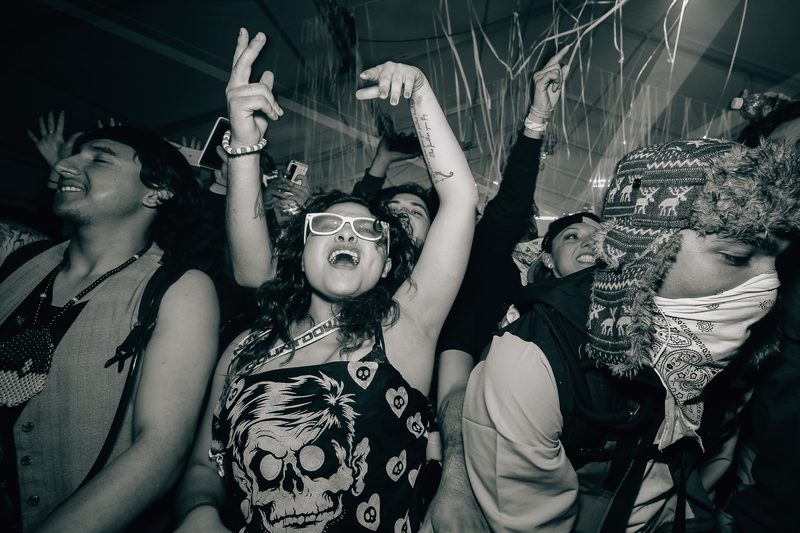 Black and white frame of a crowd dancing with arms raised at an event