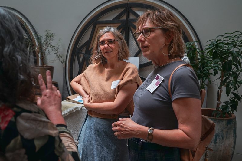 Attendees wearing name badges talking in a plant-filled room at a gathering