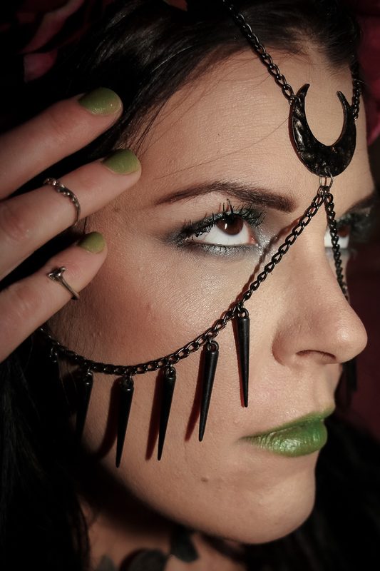 Profile view of a handmade chain headpiece worn across the cheek and brow