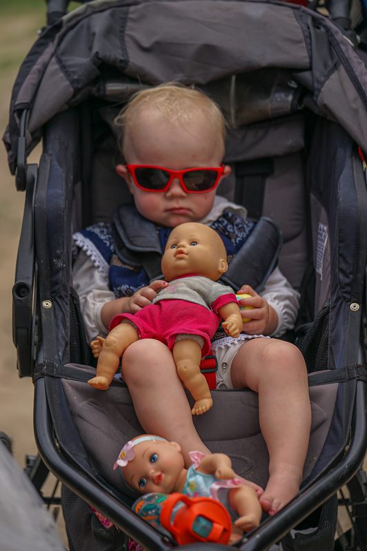 Baby in red sunglasses holding a doll in a stroller at a wedding