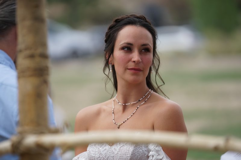 Portrait of a bride in an off-the-shoulder lace dress and layered necklace gazing off to the side