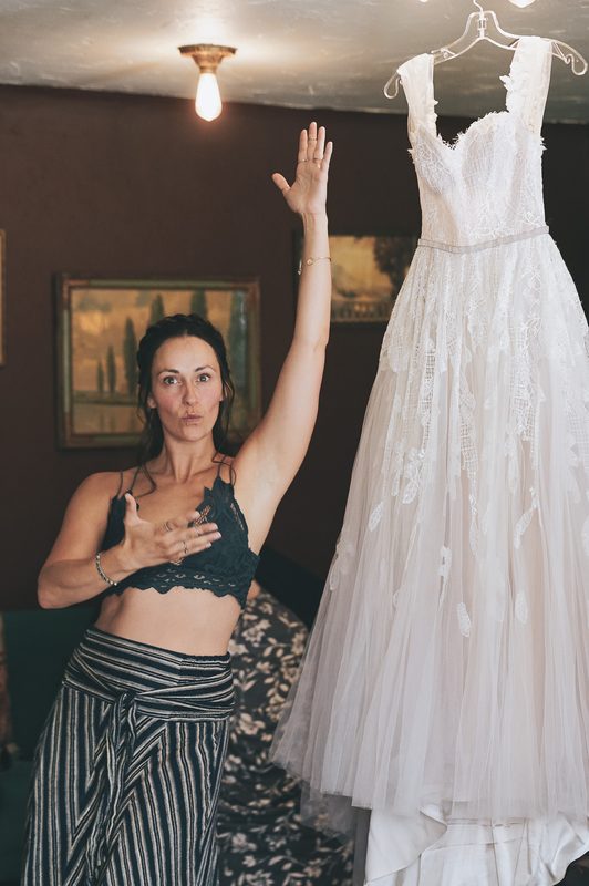 Woman with her hand on her chest standing beside a hanging wedding dress