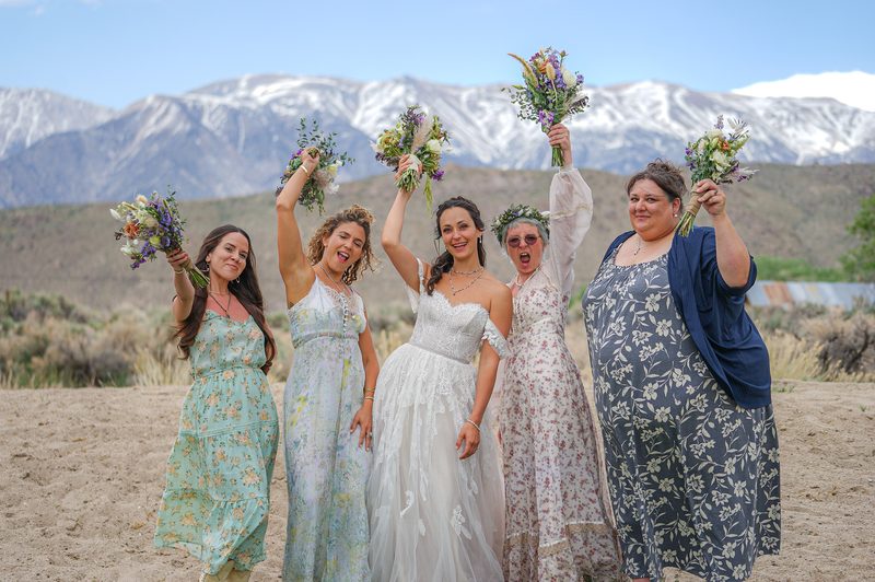 Bridesmaids and the bride raising their bouquets in celebration with snow-capped mountains behind them