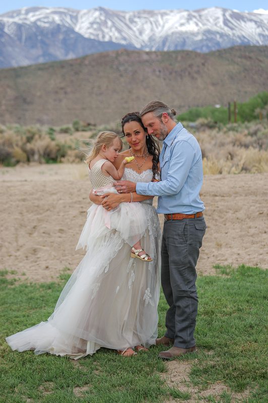 Bride and groom embracing with their flower girl in a field at a California hot spring wedding