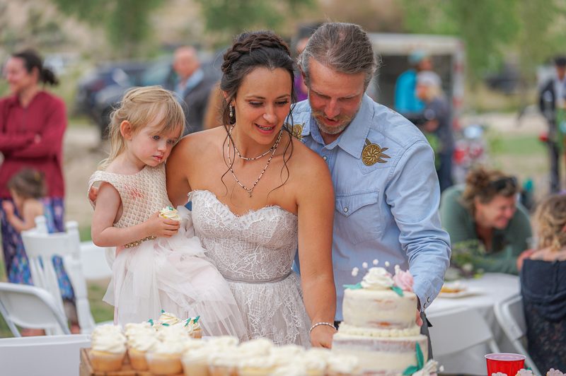 Bride, groom and flower girl leaning in to cut the wedding cake