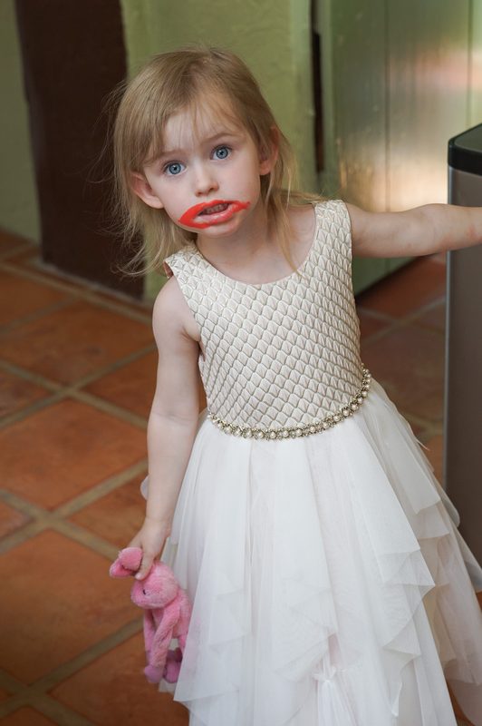Toddler flower girl in a white tulle dress with a playful lipstick smear