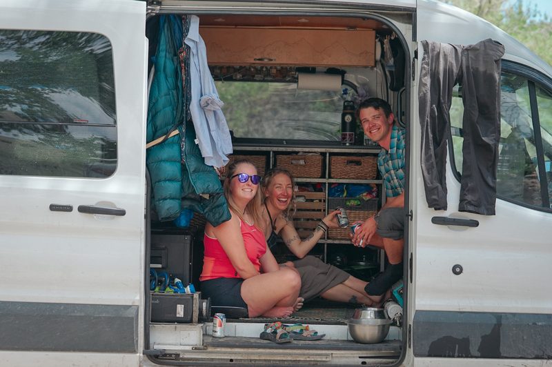Couple and a friend sitting together inside a camper van at a hot spring wedding weekend