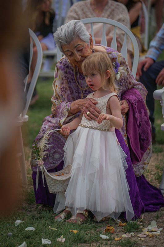 Grandmother in a purple shawl holding a flower girl during the wedding ceremony