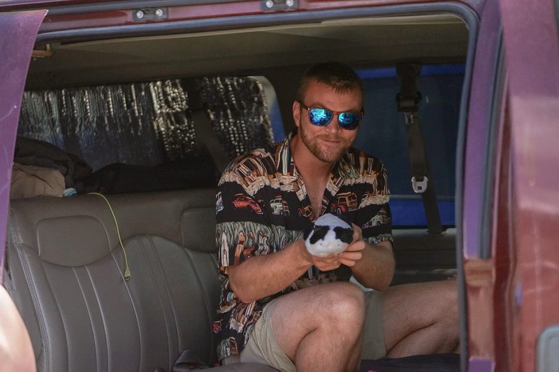 Man in mirrored sunglasses holding a small dog inside a van during a wedding weekend