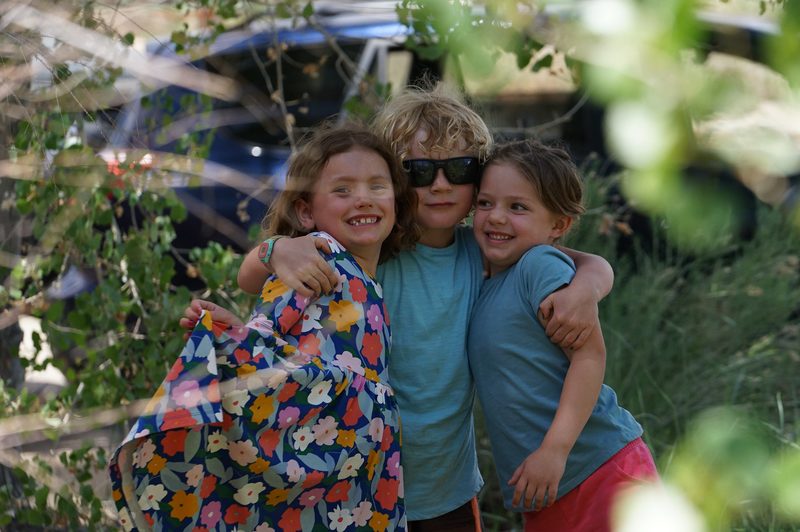 Three smiling kids hugging each other, one in a colorful floral dress, at a hot spring wedding