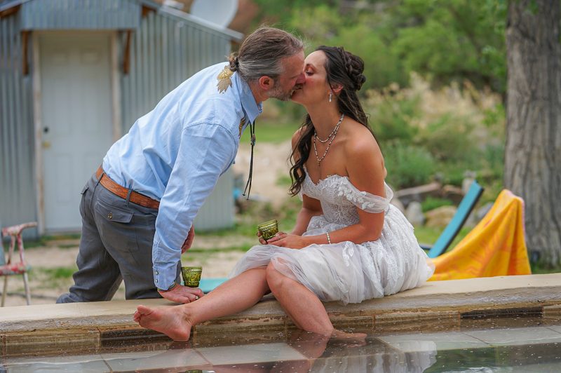 Groom kissing his bride as she sits barefoot at the edge of a hot spring