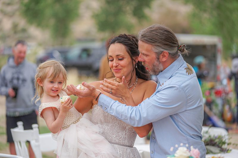 Bride and groom sharing wedding cake with their flower girl at a hot spring wedding in California