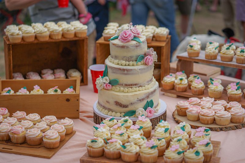Pink-flowered wedding cake surrounded by cupcakes on a dessert table