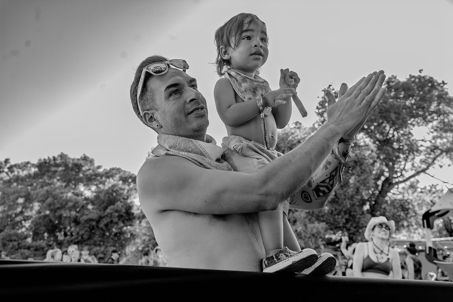 Black-and-white photo of a dad clapping while holding his toddler up to watch the music at an outdoor festival