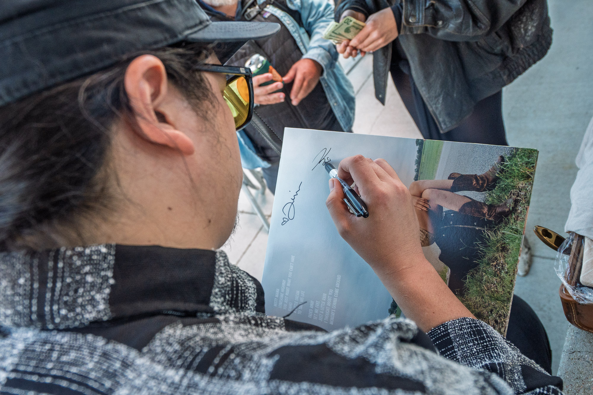A hand signs a printed photograph with a marker at the Rainy Eyes merch table, a detail from a Winter Park concert