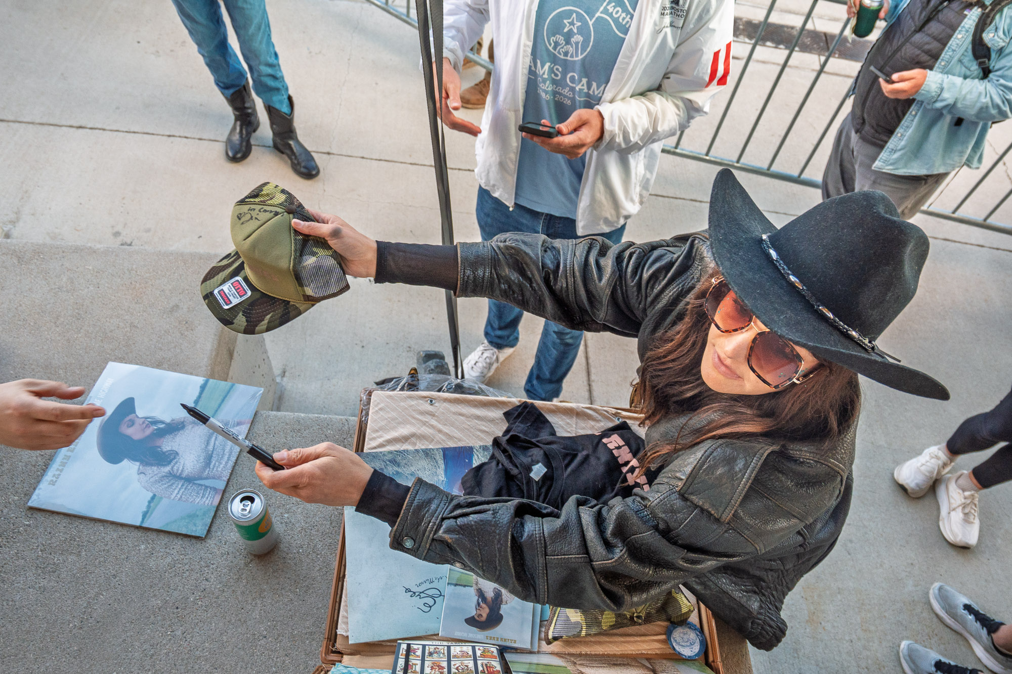 Overhead view of a Rainy Eyes member in a black hat signing photo prints at the merch table after the set