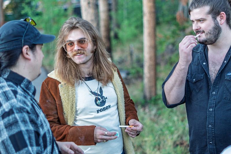 Three band members talk together in the forest between performances, behind-the-scenes tour documentary photography
