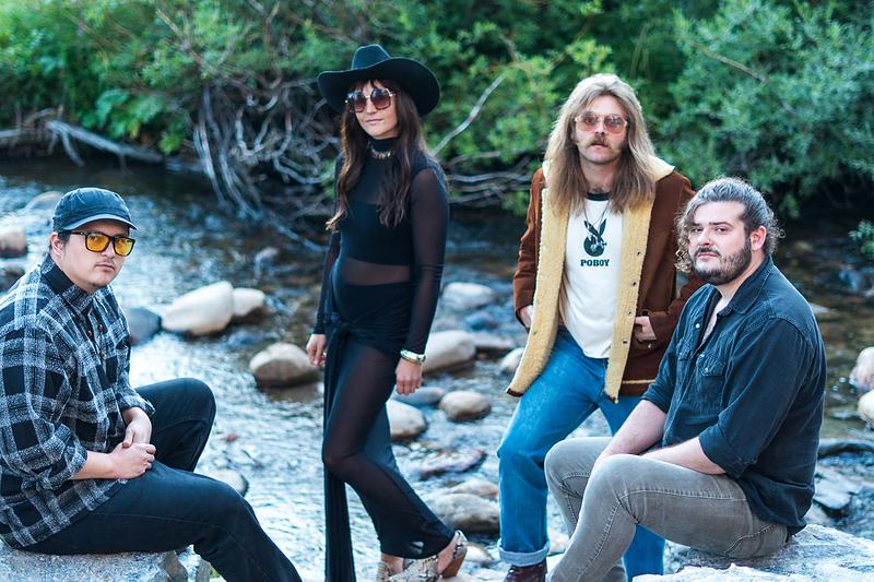 Group portrait of the four members of Rainy Eyes beside a mountain creek