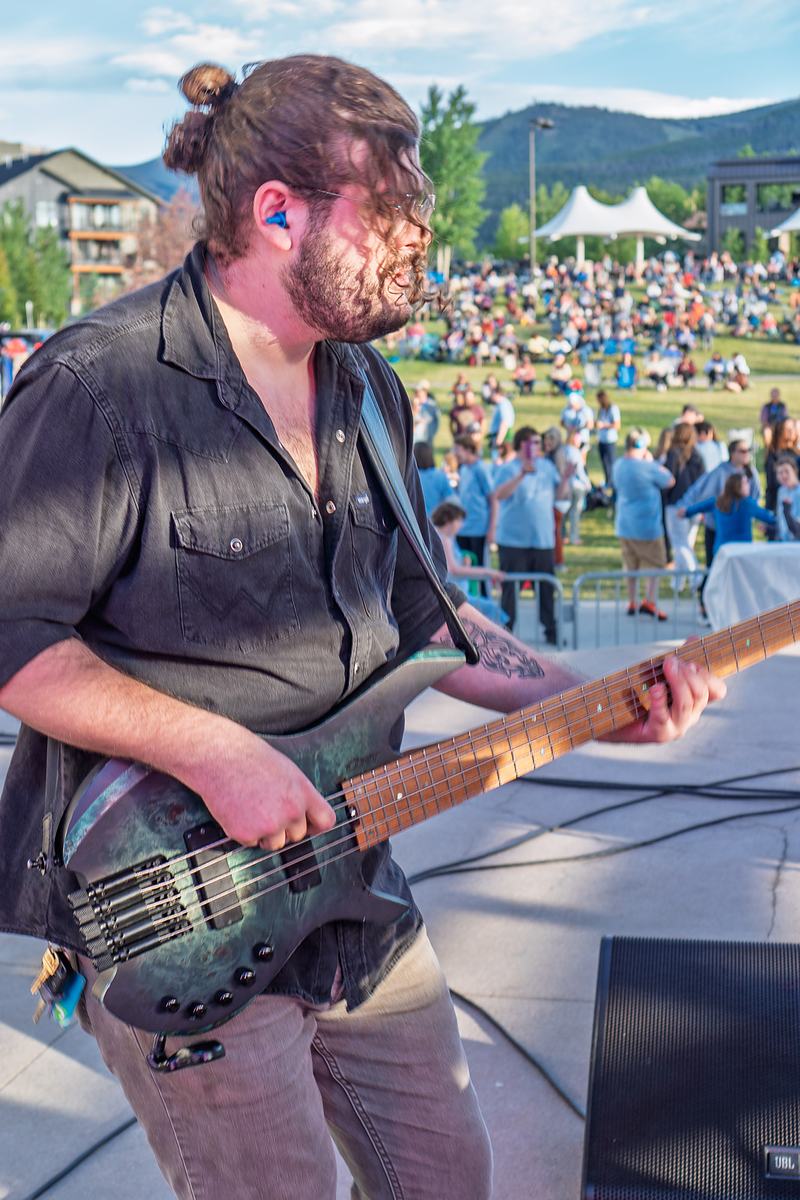 The bassist of Rainy Eyes plays on the open-air stage as the daytime crowd gathers behind, tour documentary photography by Tara Lenehan