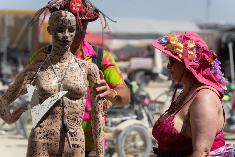 Body-painted woman beside a woman in a pink flower hat at Burning Man