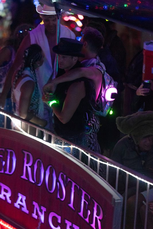 Couple embracing in glowing night lights beside a red neon sign at Burning Man