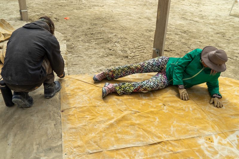 Volunteers kneeling and laying a large yellow tarp across the dusty playa floor at Burning Man