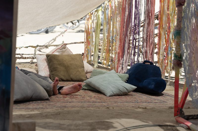 Cushions and colorful hanging streamers in a shaded camp lounge at Burning Man