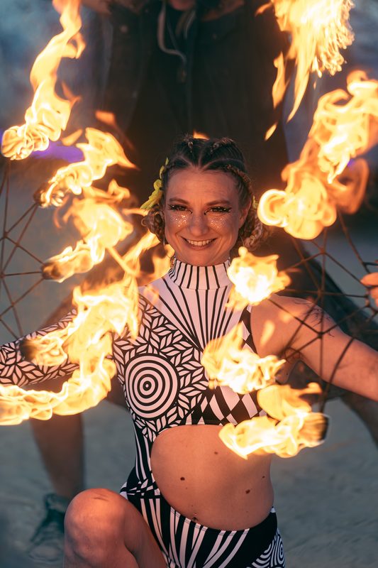 Performer in a black and white outfit with flaming fans at Burning Man