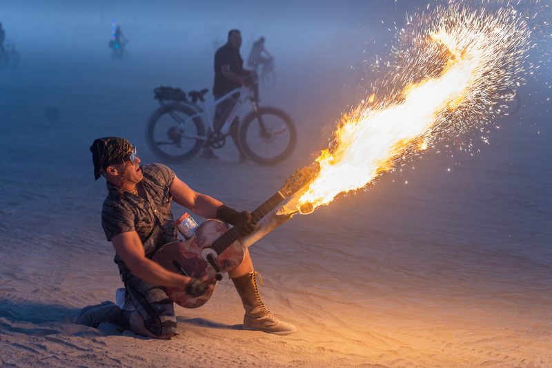 Performer crouching and sending a plume of flame into the night sky at Burning Man