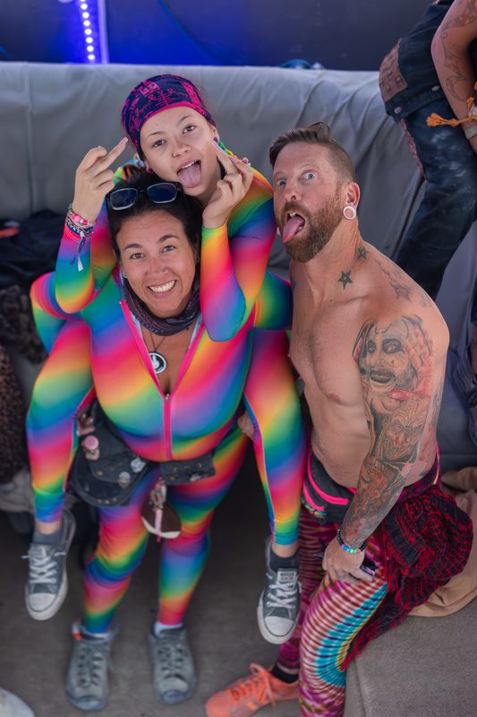 Two friends in rainbow-colored outfits laughing and looking up at the camera at Burning Man