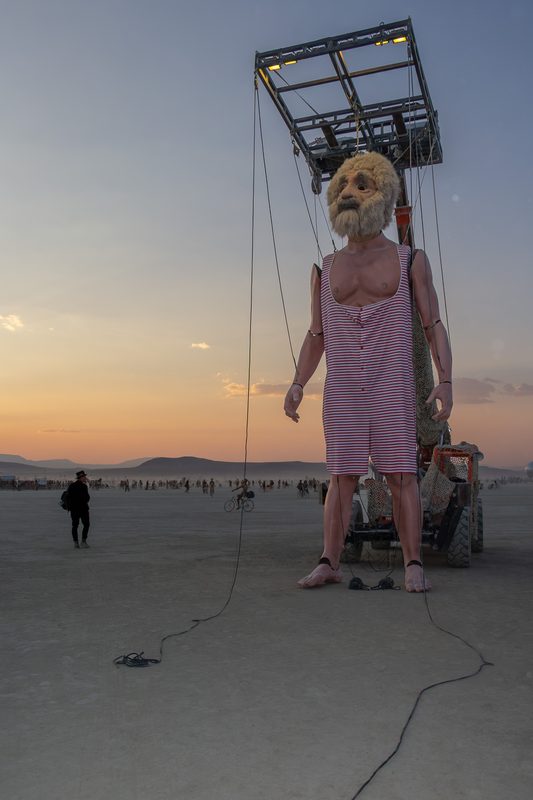 Giant figure in a pink dress suspended from a crane at sunset at Burning Man