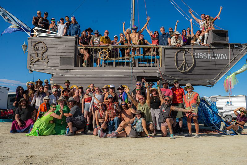 Large group of people posing on and around a ship-shaped art car at Burning Man