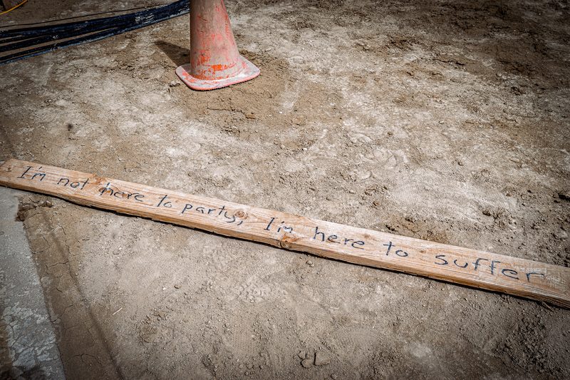 Close-up of a handwritten wooden board lying on cracked playa ground beside an orange cone at Burning Man