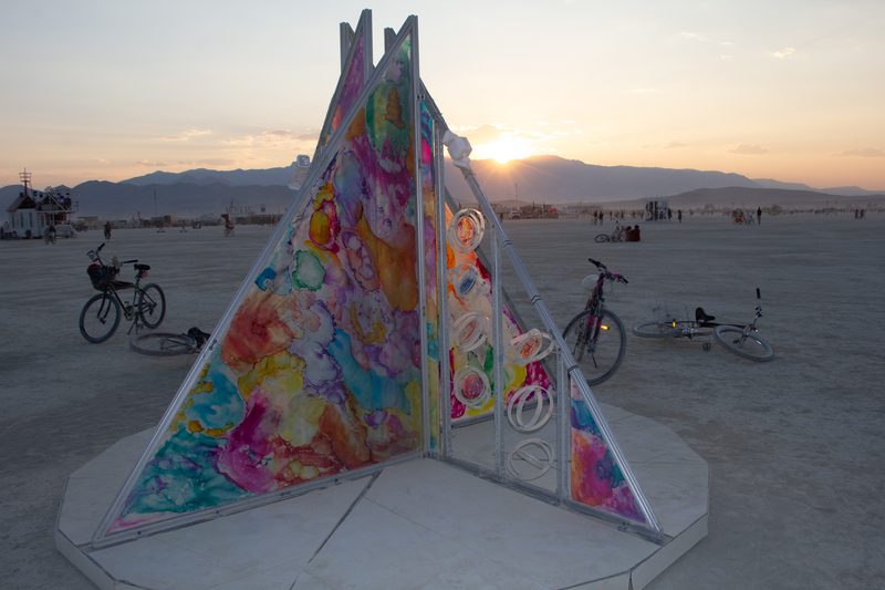Colorful hand-painted tent-shaped sculpture at sunset on the playa at Burning Man