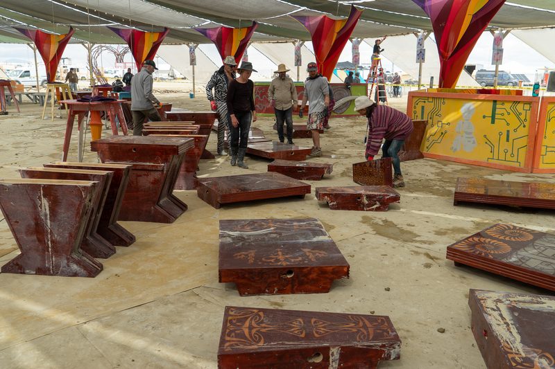 Red wooden panels laid out across the floor of a large shade structure with crew at work at Burning Man