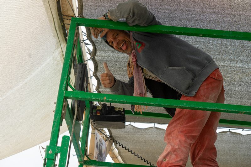 Smiling crew member giving a thumbs up from a green scaffold lift at Burning Man