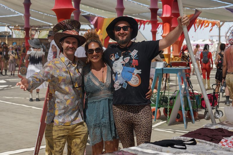 Three friends posing together in colorful costumes on a street at Burning Man
