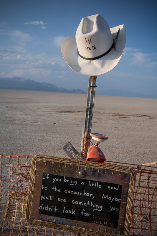 White cowboy hat mounted on a pole above a chalkboard sign on the playa at Burning Man