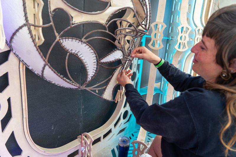 Woman smiling as she attaches a decorative piece to an ornate sculpted art panel at Burning Man