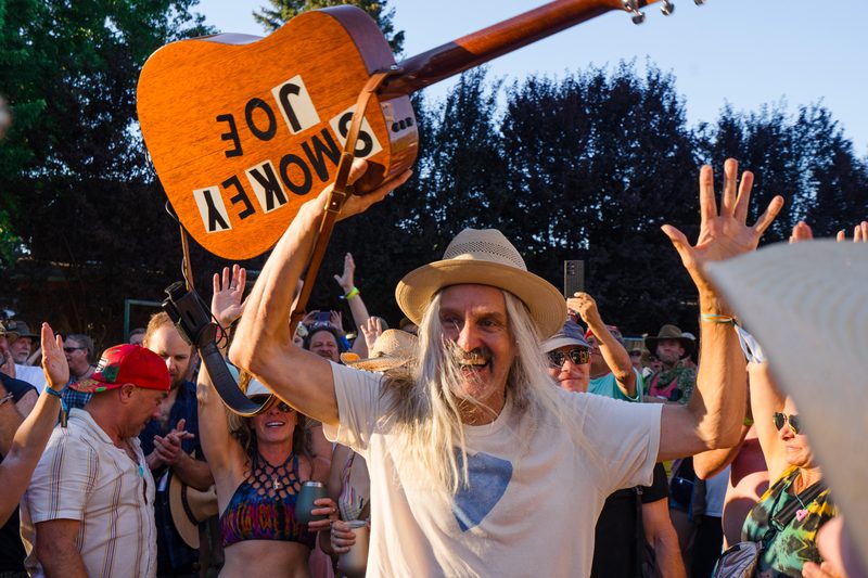 Festival-goer in a straw hat holding up a guitar-shaped sign in a cheering crowd