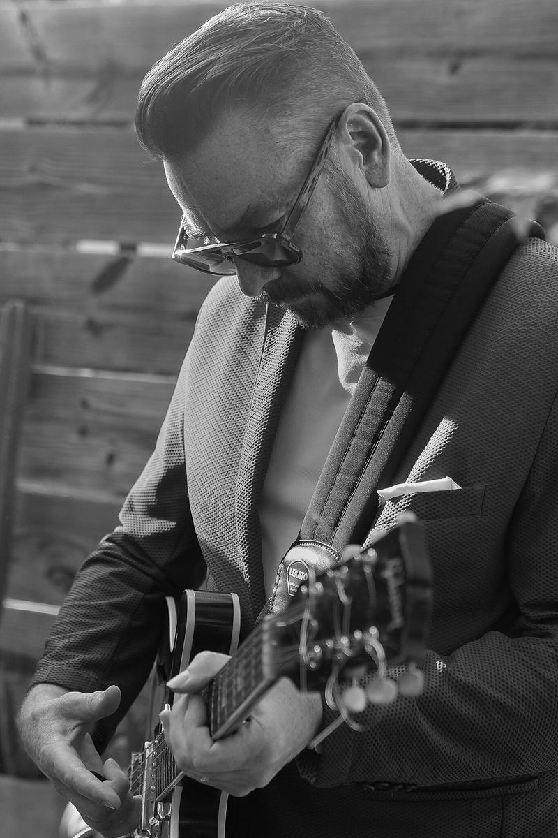 Black and white photograph of a man in glasses playing acoustic guitar at a live jazz performance