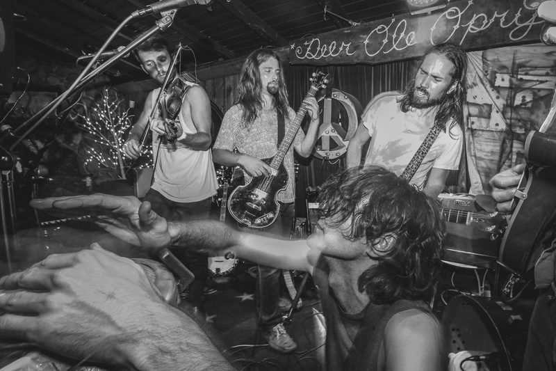 Black and white photo of a band performing on a cramped club stage with motion-blurred hands in the foreground during an Insects vs. Robots show
