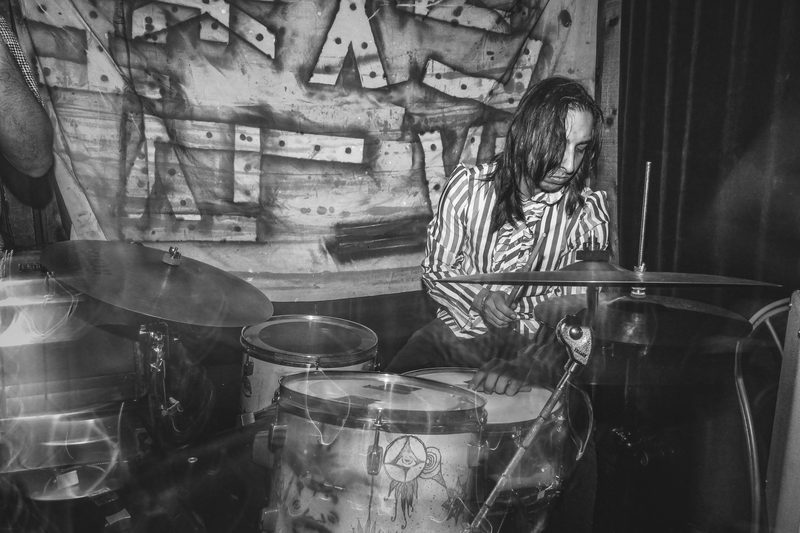 Black and white photo of a drummer in a striped shirt behind his kit during an Insects vs. Robots show
