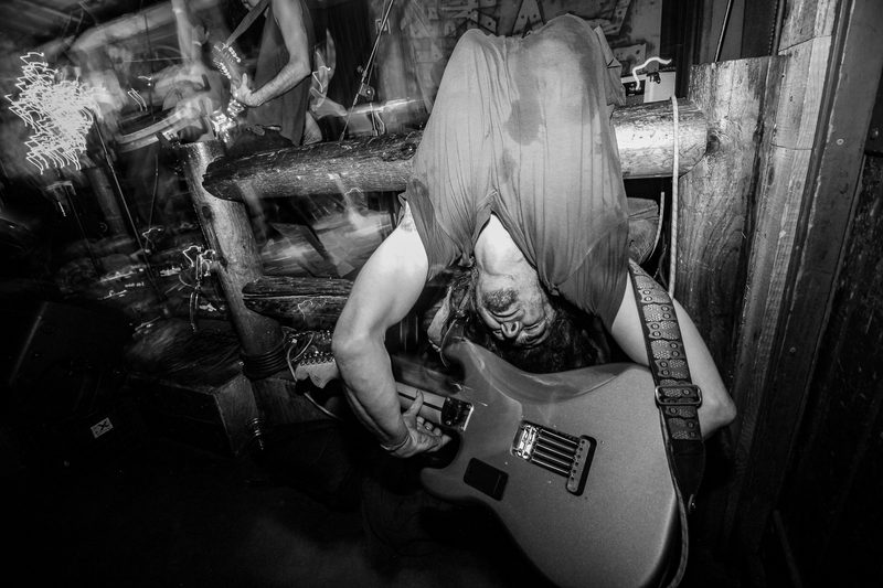 Black and white photo of a guitarist bent over with long hair covering his face during an Insects vs. Robots show