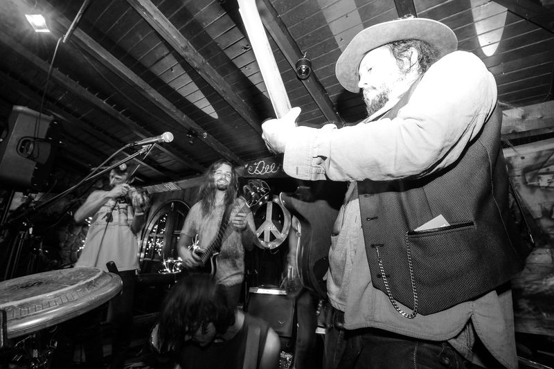 Black and white photo of a guitarist in a wide-brim hat playing in a dim venue during an Insects vs. Robots show