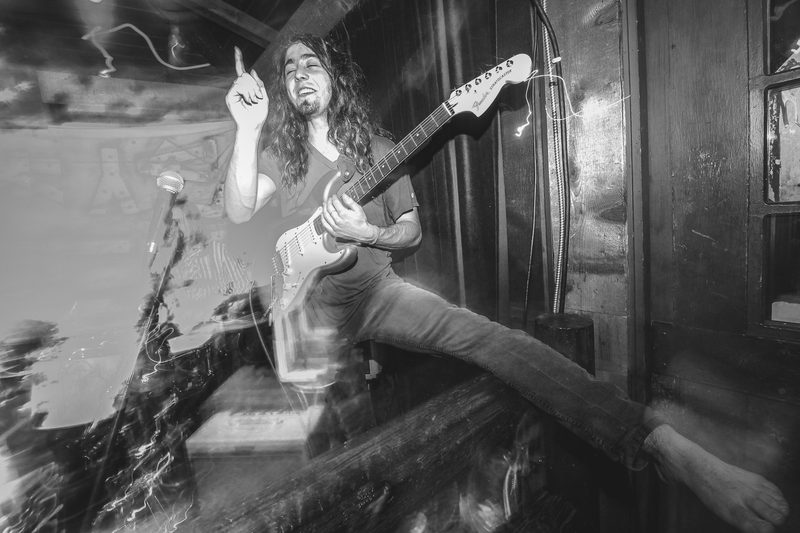 Black and white photo of a guitarist leaping across the stage mid-song during an Insects vs. Robots show