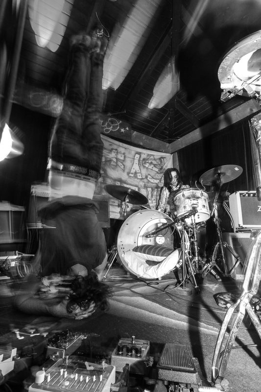 Black and white photo of a performer upside down in a headstand in front of a drum kit during an Insects vs. Robots show